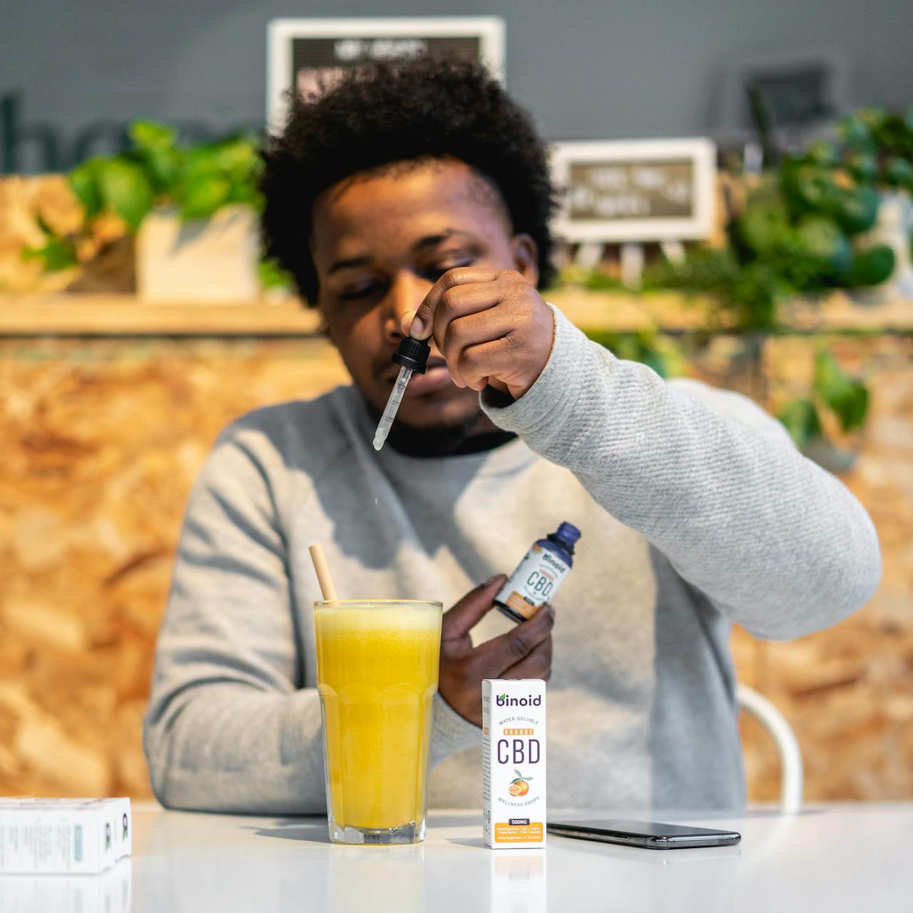 Man adding Binoid water-soluble CBD oil drops into a glass of orange juice using a dropper
